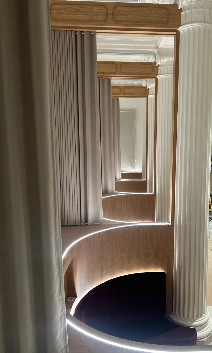 Curved oak booths lit from below, seen through a doorway between white period columns